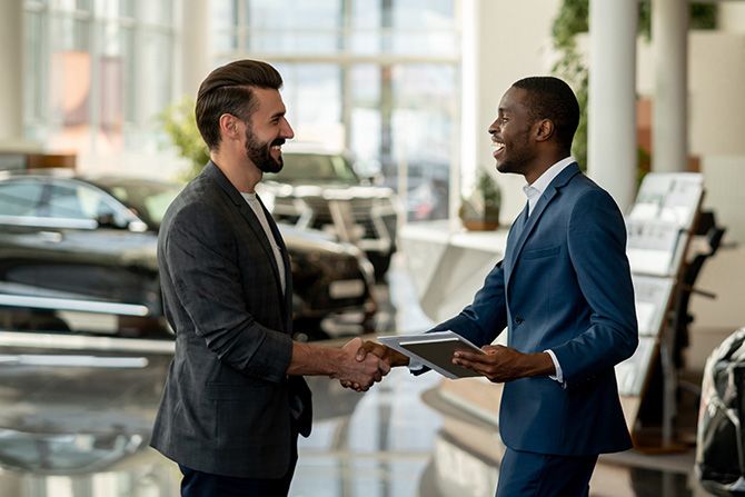 Two Business Men in a Dealership showroom shaking hands and holding paperwork