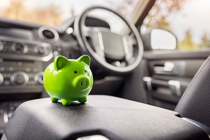 Green piggy bank sitting on the center console of a vehicle with the steering wheel and controls blurred in background